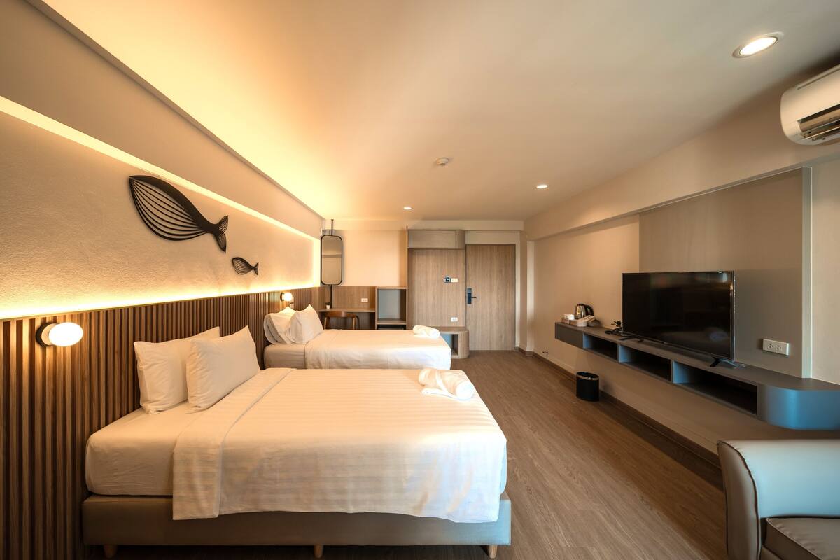 A hotel room with two beds, a TV, a desk, and a wall-mounted shelf.