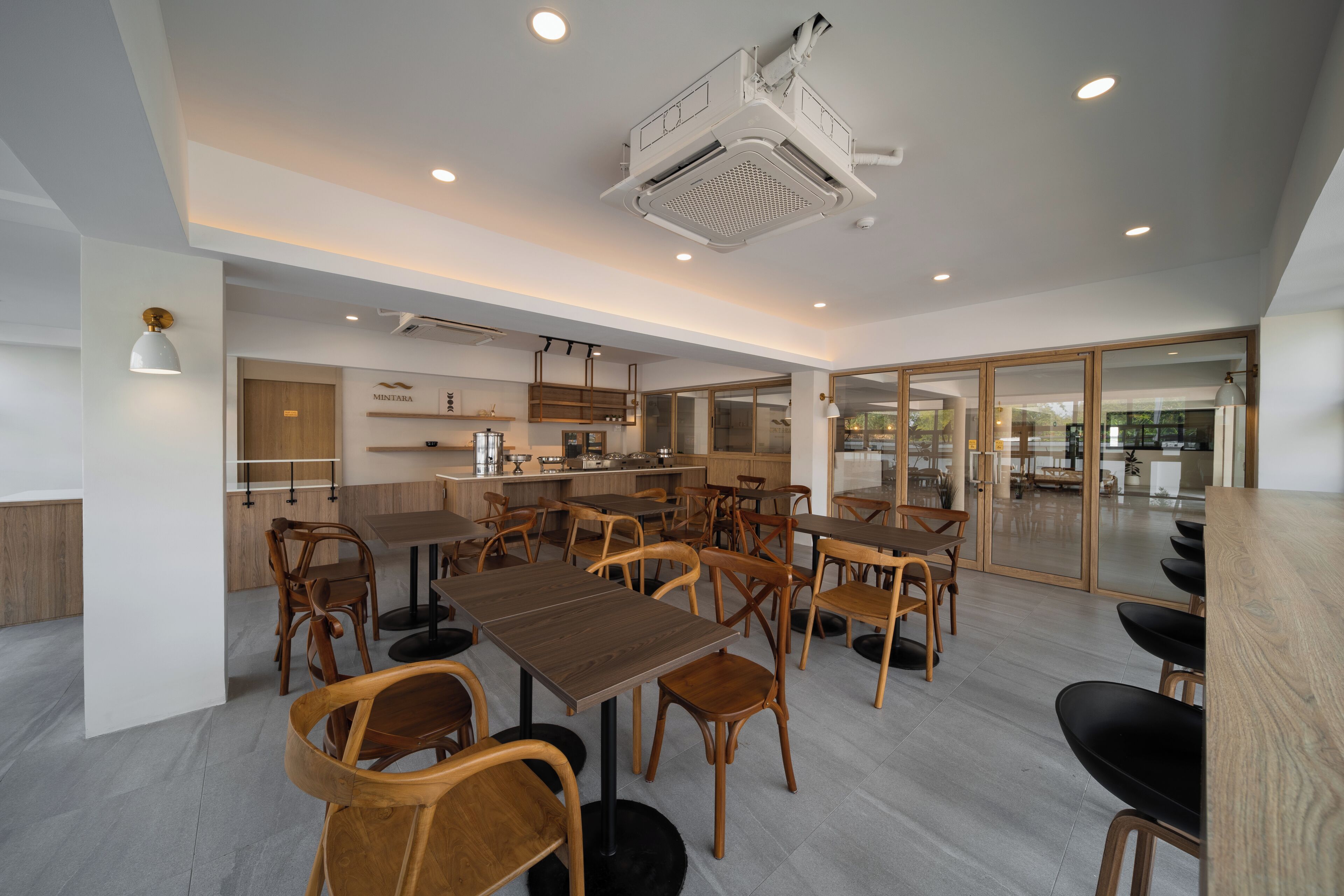 A modern restaurant with wooden tables and chairs, a kitchen area, and large windows.