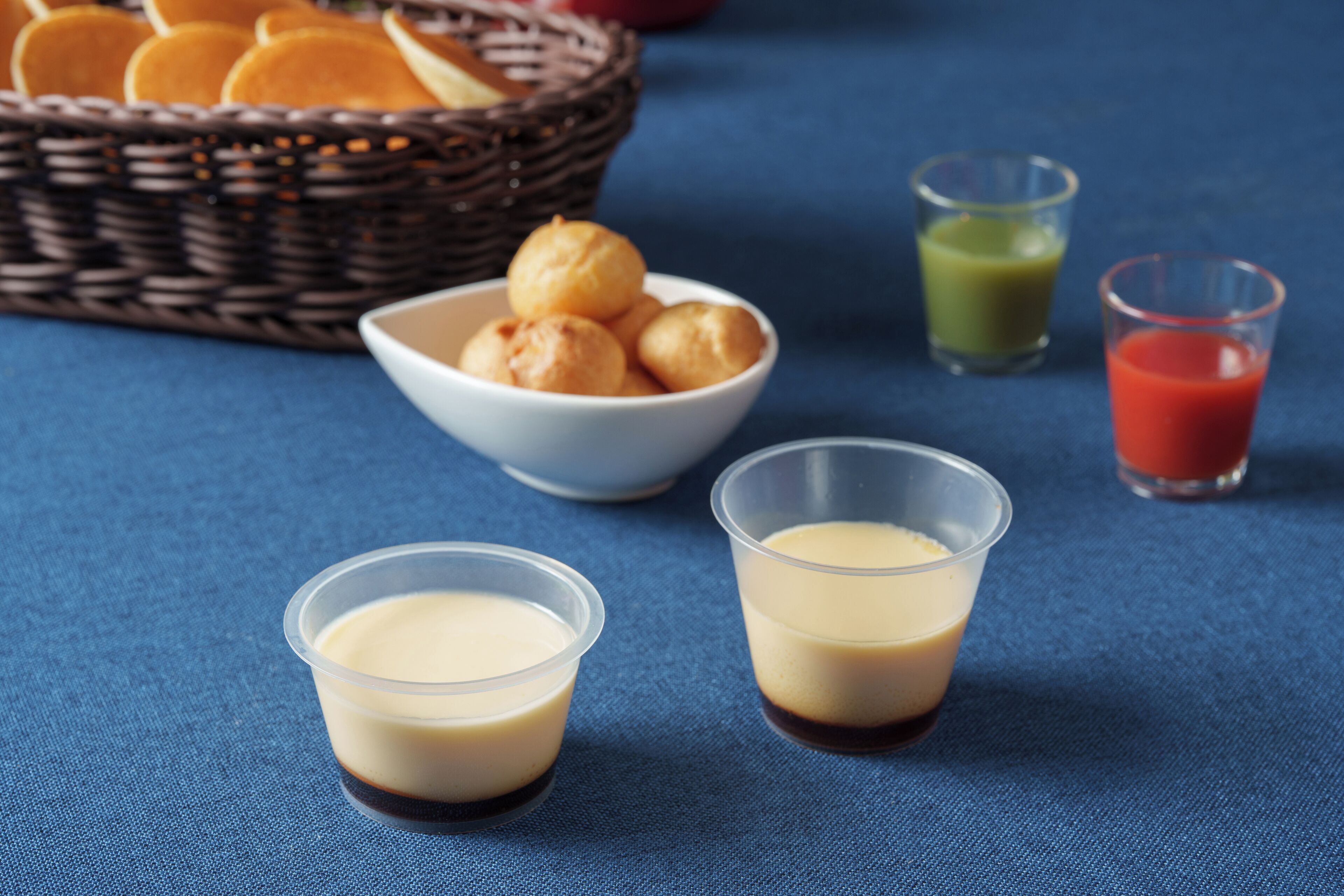 A table with a basket of bread, a bowl of sweets, and two glasses of a creamy beverage.