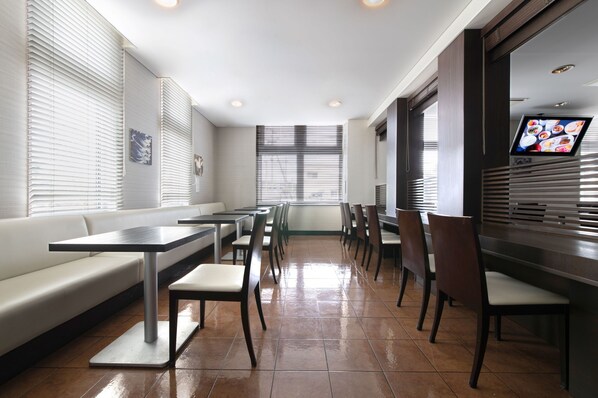 A modern restaurant with a long counter, booths, and a TV screen.