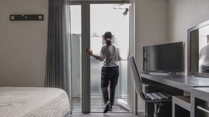 Une chambre d’hôtel comprenant un lit, un bureau avec une chaise, une télévision et une porte-fenêtre coulissante donnant sur un balcon.