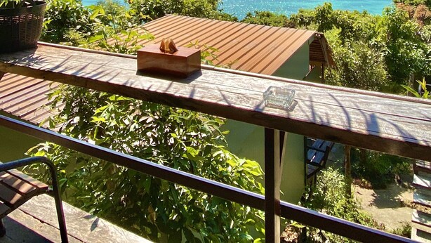Varanda com telhado de palha com vista para um mar azul-turquesa e montanhas ao longe.
