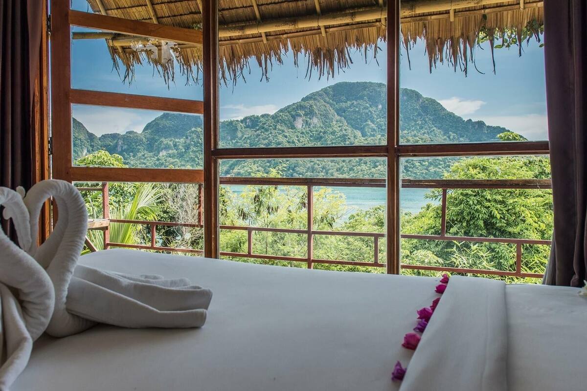 Une chambre d’hôtel dotée d’une grande fenêtre donnant sur un paysage de montagnes verdoyantes et un lac.