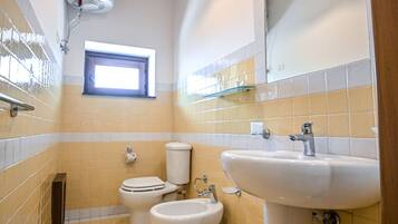 Un baño con inodoro, bidé y lavamanos. Hay una ventana sobre el inodoro y un espejo sobre el lavamanos.