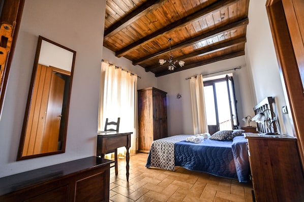 A bedroom with a wooden ceiling, a bed with a patterned bedspread, a desk, and a chair. - Il Ciliegio dell'Etna (Giarre)