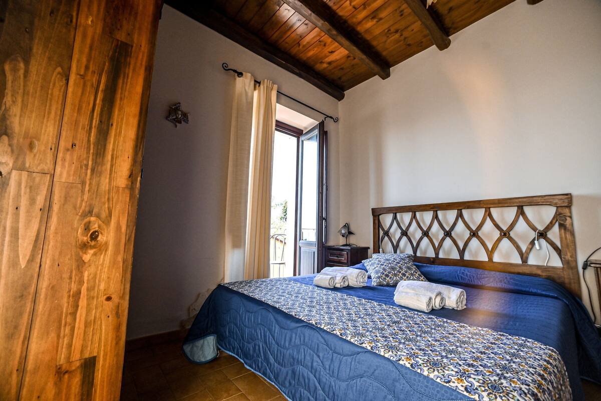 A bedroom with a wooden ceiling, a bed with a blue quilt, and a nightstand.