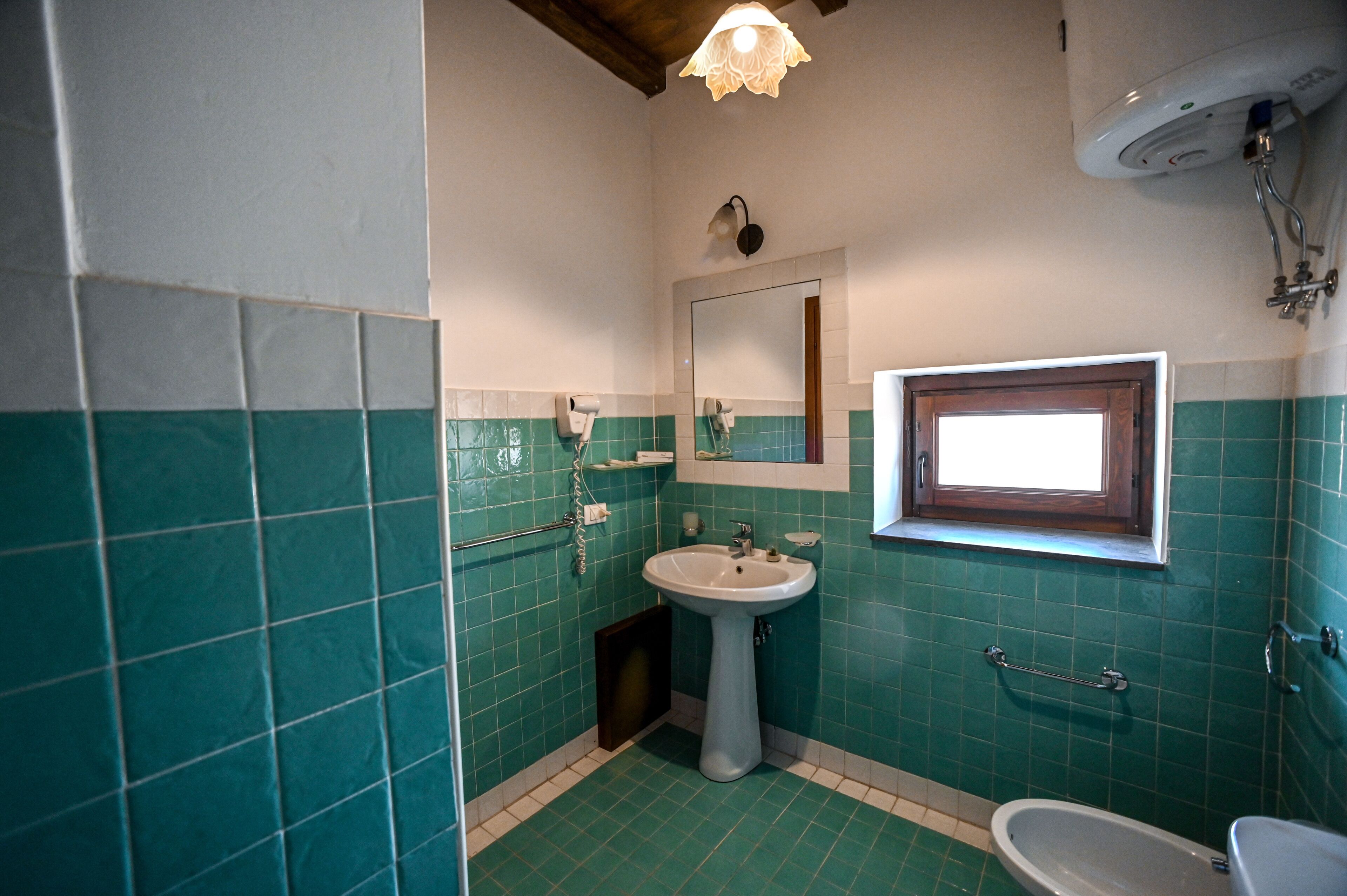 A bathroom with a pedestal sink, a mirror, a window, and a shower.