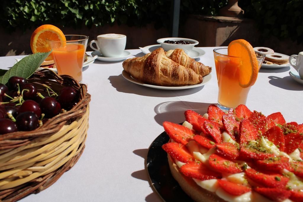 A breakfast setting with a basket of cherries, a plate of strawberries, a croissant, a glass of orange juice, and a cup of coffee.