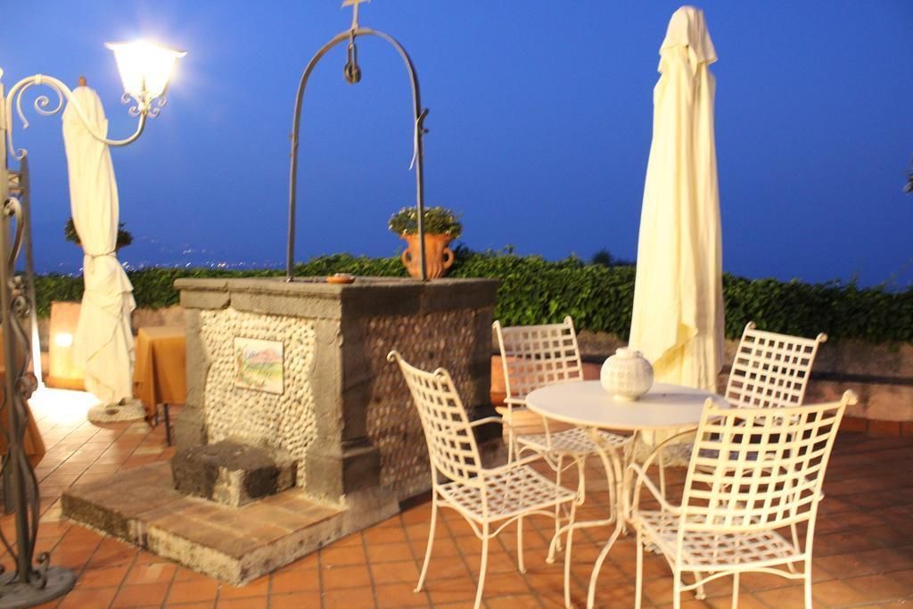 An outdoor patio with a stone fireplace, white metal chairs, and a table.