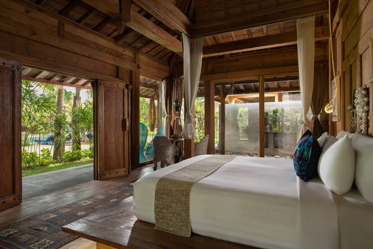 Una habitación de madera con una cama, cortinas y vistas al verde exterior.