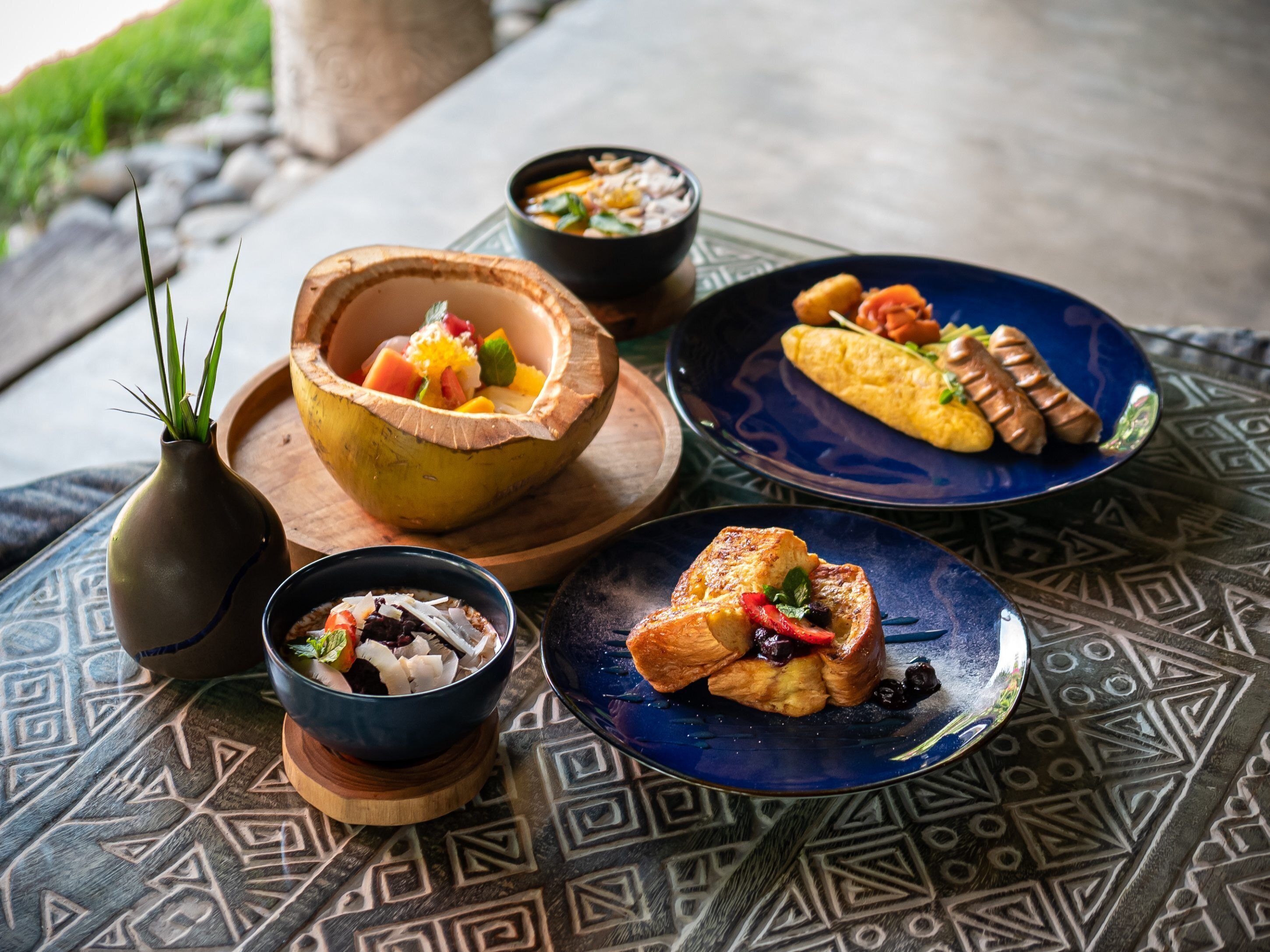A table with various dishes, including a bowl of fruit, a plate of sausages, and a bowl of soup.