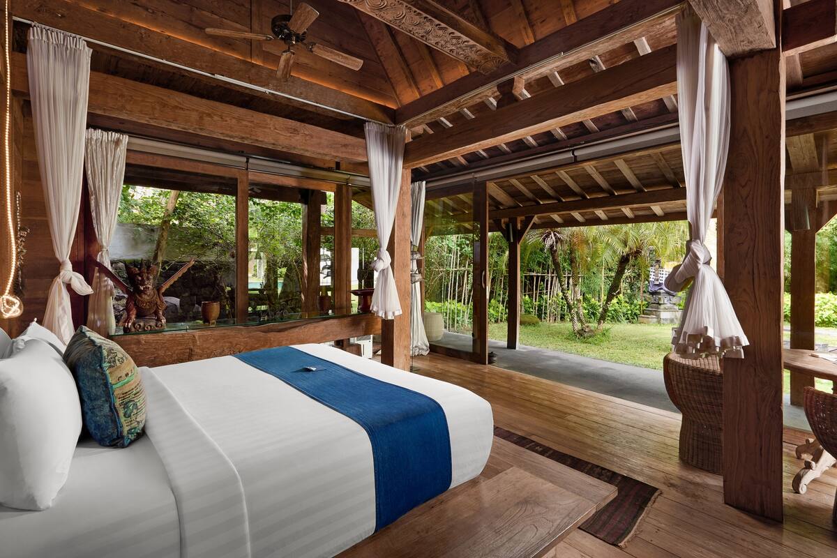 Un dormitorio con una cama grande, vigas de madera en el techo y vistas al jardín.