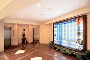 A lobby with a large information board, elevators, and potted plants.
