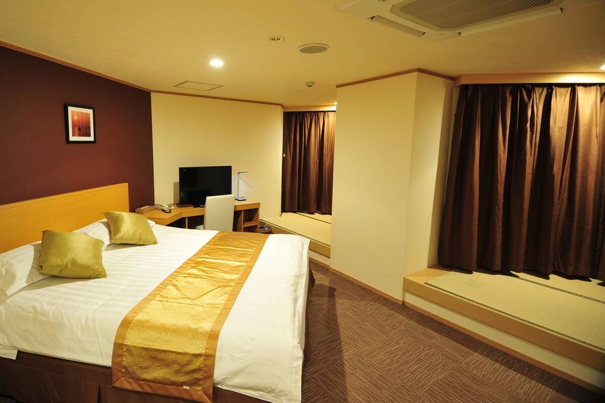 Une chambre d’hôtel avec un grand lit, un bureau avec un ordinateur, une télévision et une fenêtre avec des rideaux.