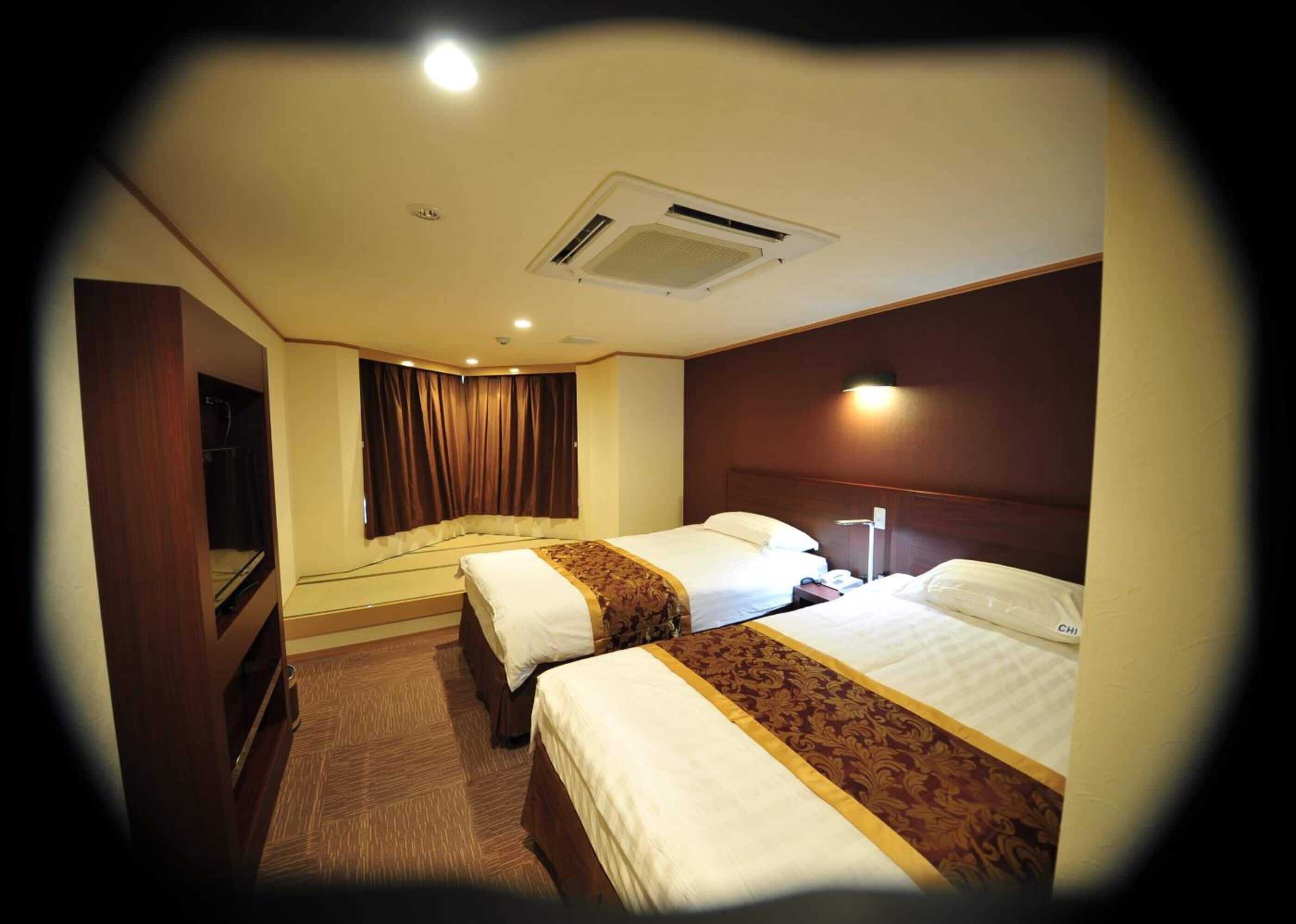 A hotel room with two beds, a wardrobe, a desk, and a window with curtains.