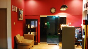 A room with a red wall, a brown sofa, a bookshelf, and a door leading to a garden. - Rumi Apartelle Hotel (Angeles City)