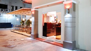 A modern building with a glass entrance, a covered outdoor seating area, and a visible interior with a counter and seating. - Rumi Apartelle Hotel (Angeles City)