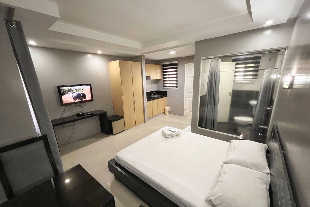 Une chambre d’hôtel moderne équipée d’un lit, d’une télévision, d’un bureau, d’une armoire et d’une salle de bain visible à travers une porte en verre.