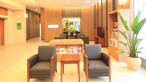 A reception area with a wooden reception desk, two armchairs, a coffee table, and a bookshelf with magazines. - Vessel Inn Sapporo Nakajima Park (Sapporo)