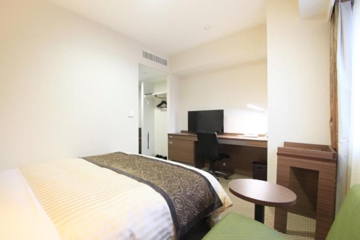 A hotel room with a bed, a desk with a computer, a chair, and a small table.