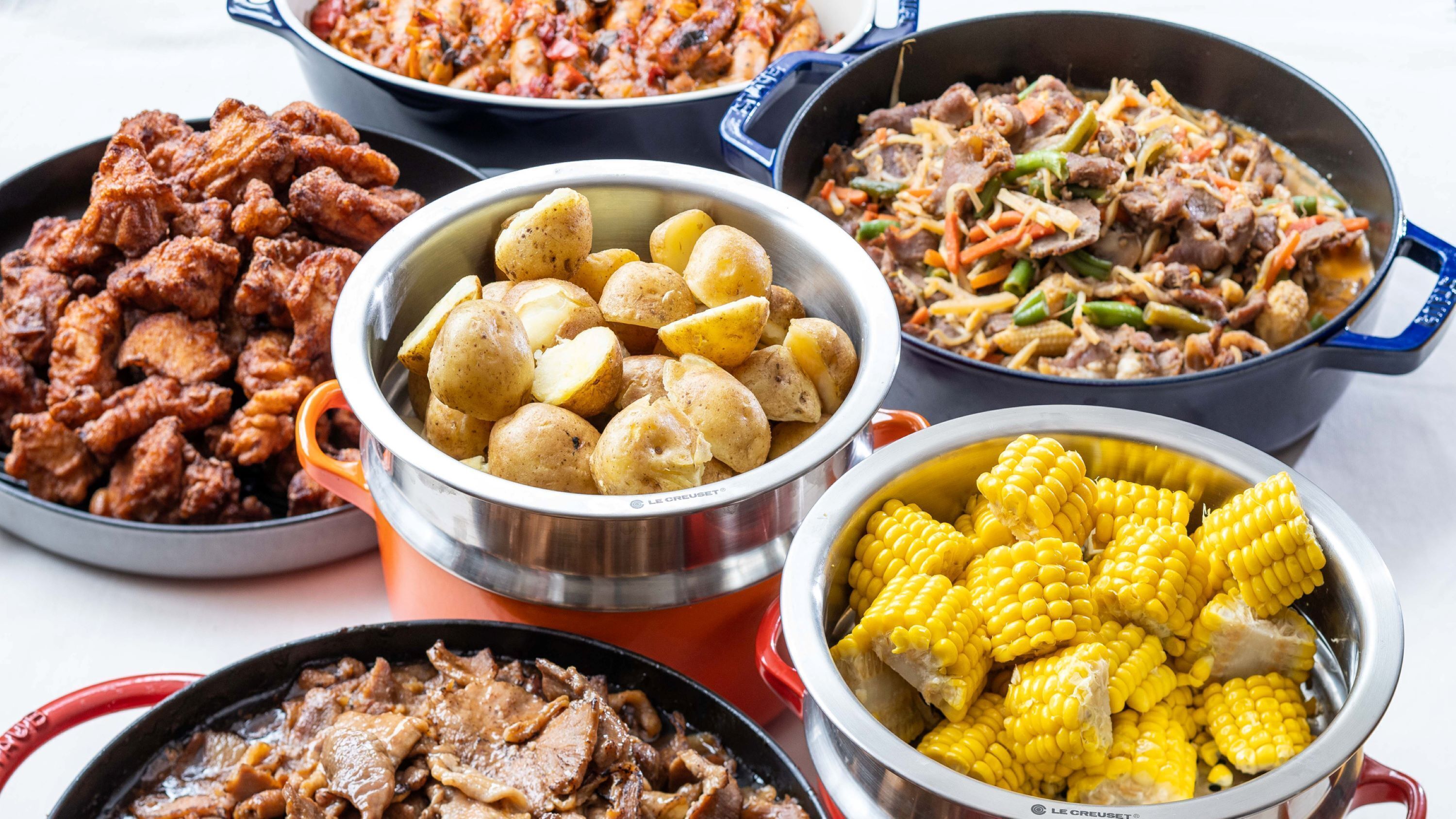 A variety of dishes including fried chicken, roasted potatoes, and corn on the cob.