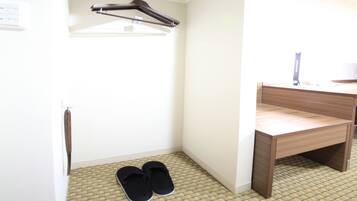 A small room with a wooden desk, a hanging clothes rack, and a pair of slippers on the floor.