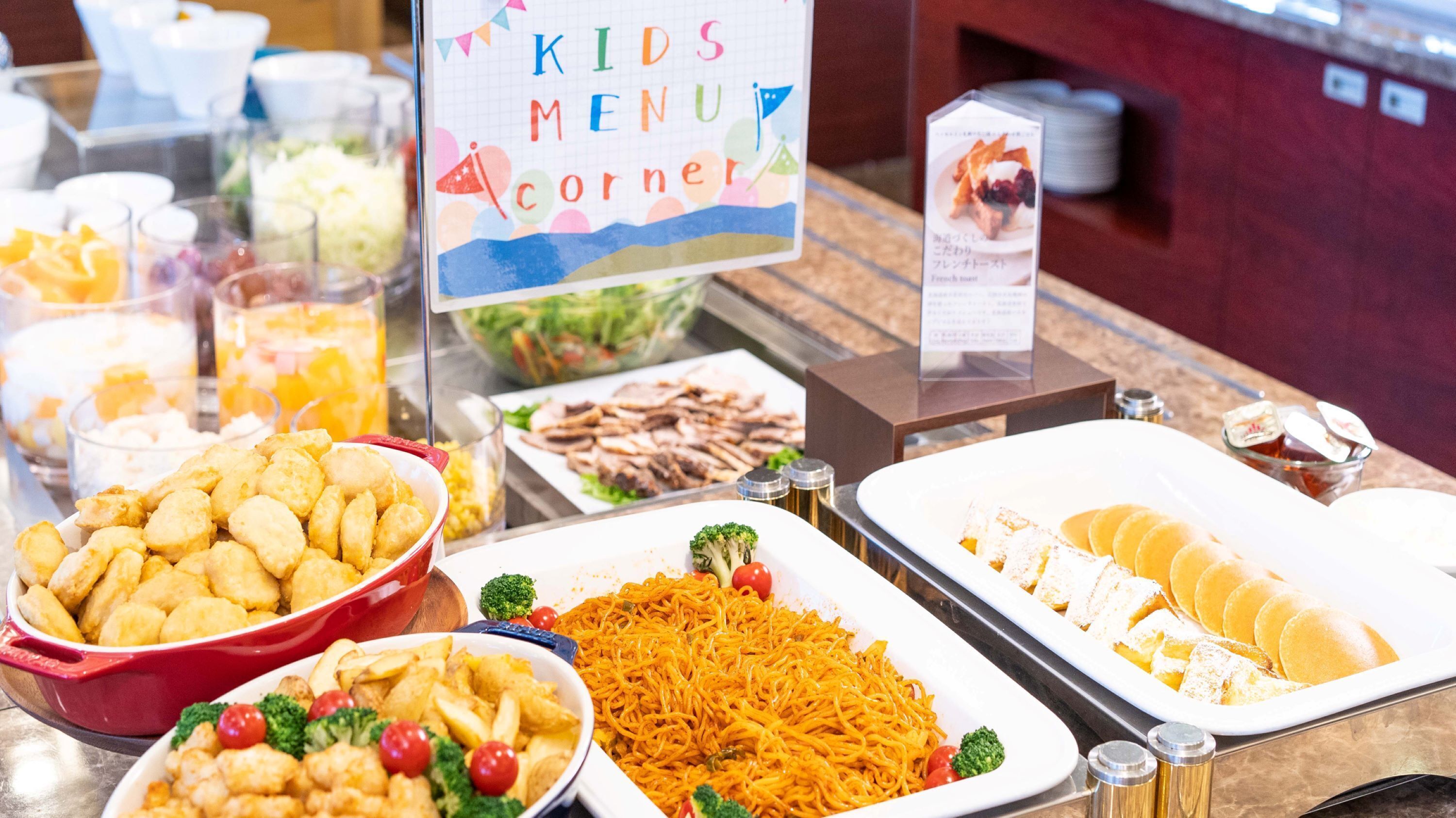 A buffet with various dishes including fried items, noodles, and salads, labeled as "KIDS MENU CORNER".