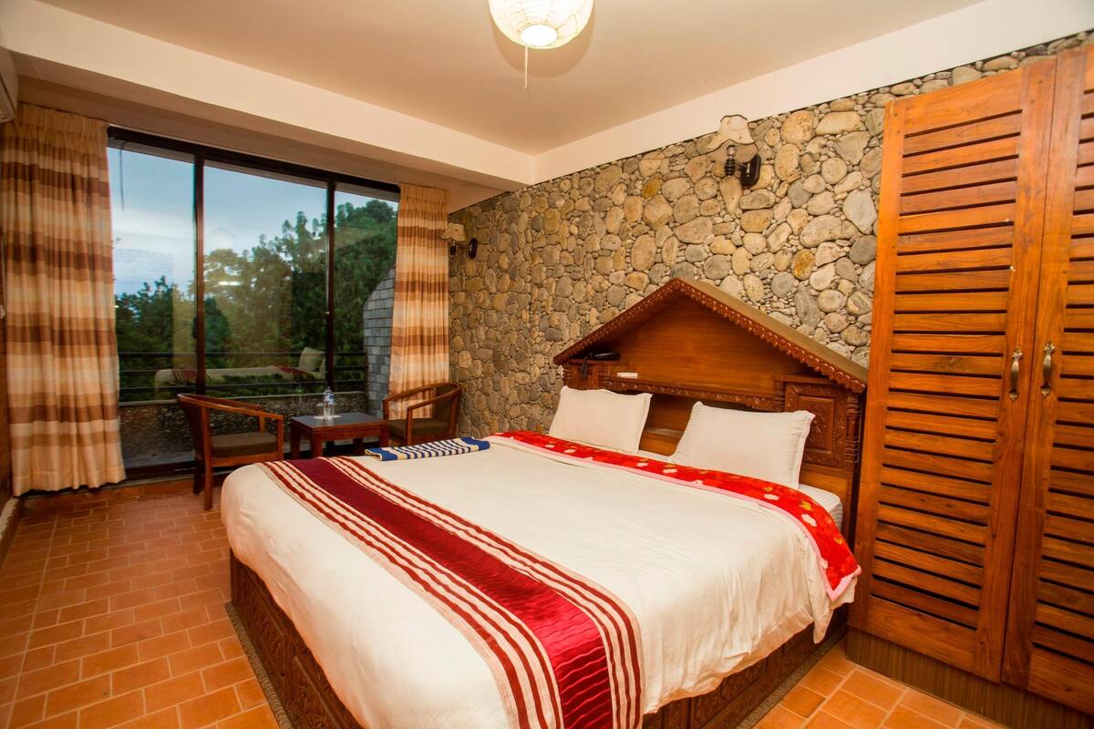 Quarto com uma cama grande, parede de pedra, cabeceira de madeira, guarda-roupa de madeira e porta de vidro deslizante para uma varanda.