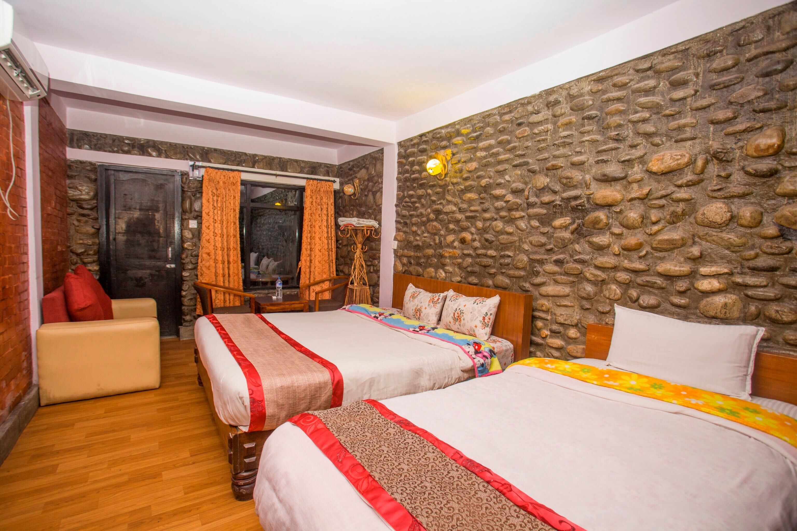 A room with two beds, a stone wall, a wooden floor, and a small seating area.