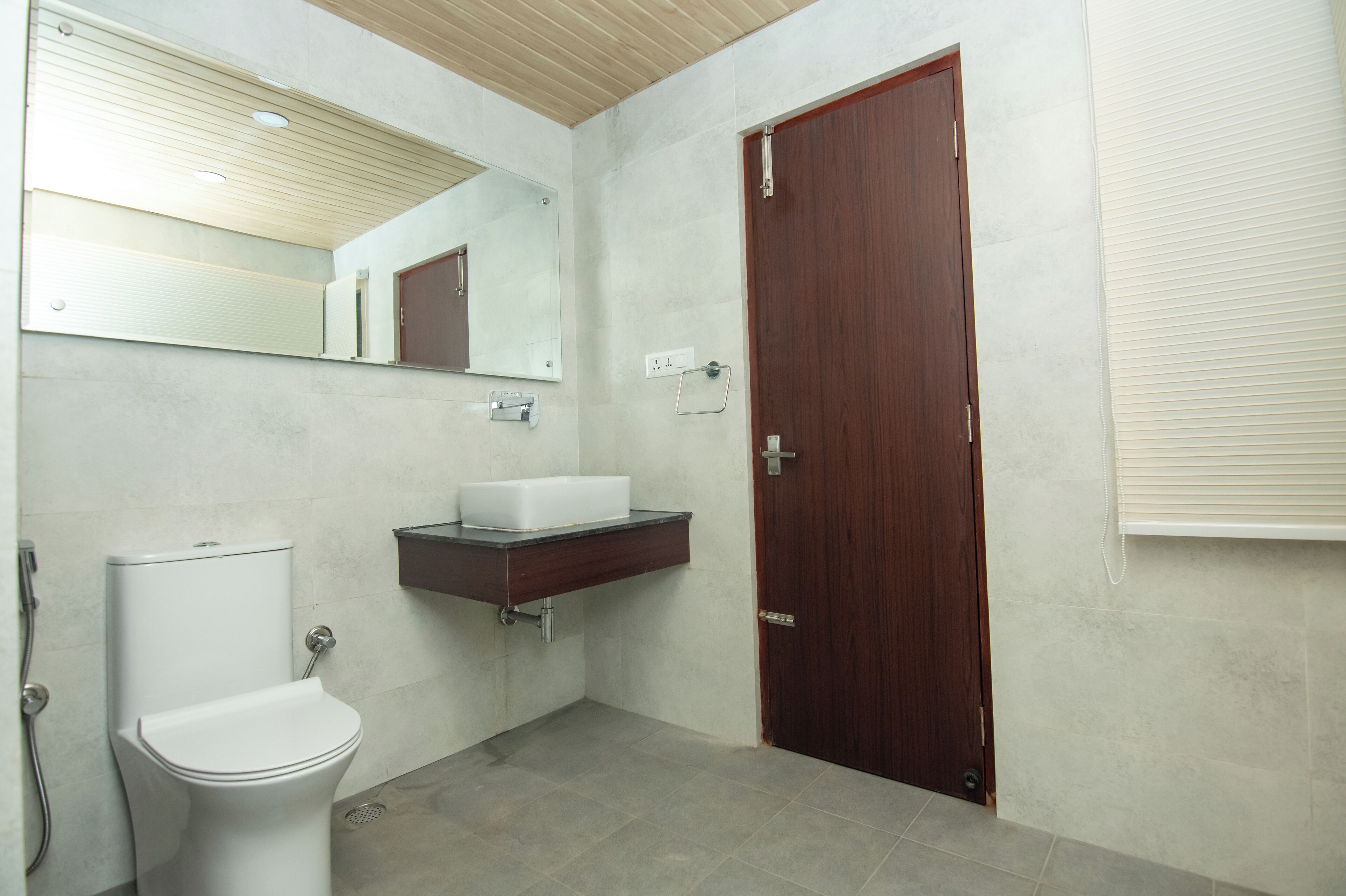 A bathroom with a toilet, a sink, a mirror, and a wooden door.