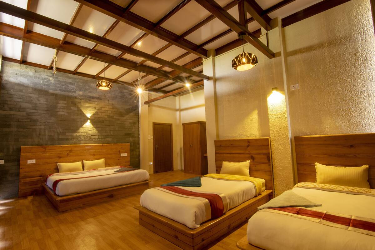 Quarto de hotel com três camas de madeira, parede de pedra e teto de madeira.