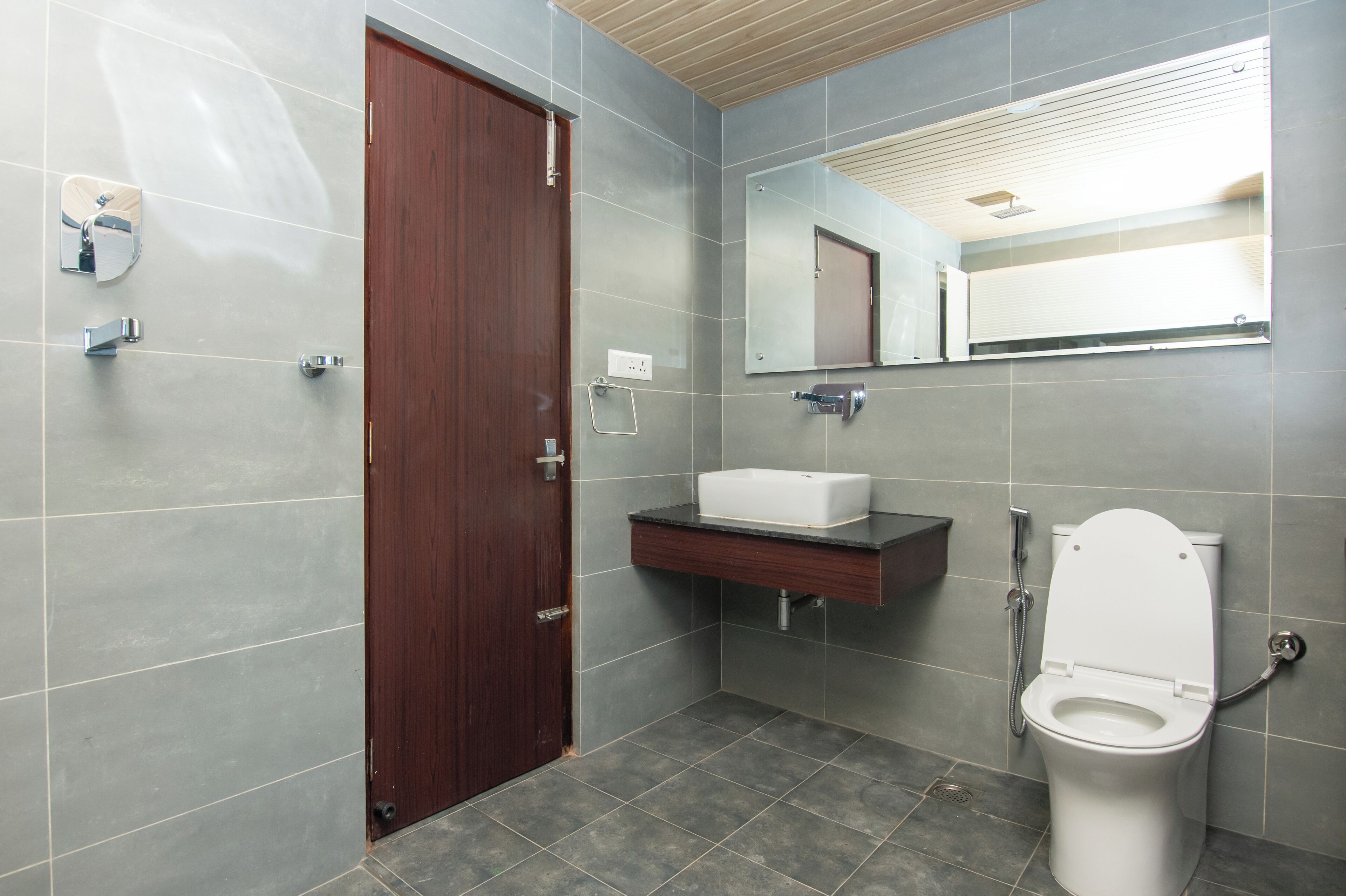 A modern bathroom with a wooden door, a white sink, and a toilet.