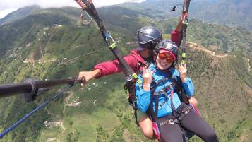 Dues persones fent parapent sobre un paisatge muntanyós amb camps de conreu terrassats a la part inferior.