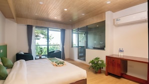 Ein modernes Hotelzimmer mit einem großen Bett, einer Holzbalkendecke, einer Glastür, die auf einen Balkon führt, und einem Holztisch mit einer Wasserflasche darauf.