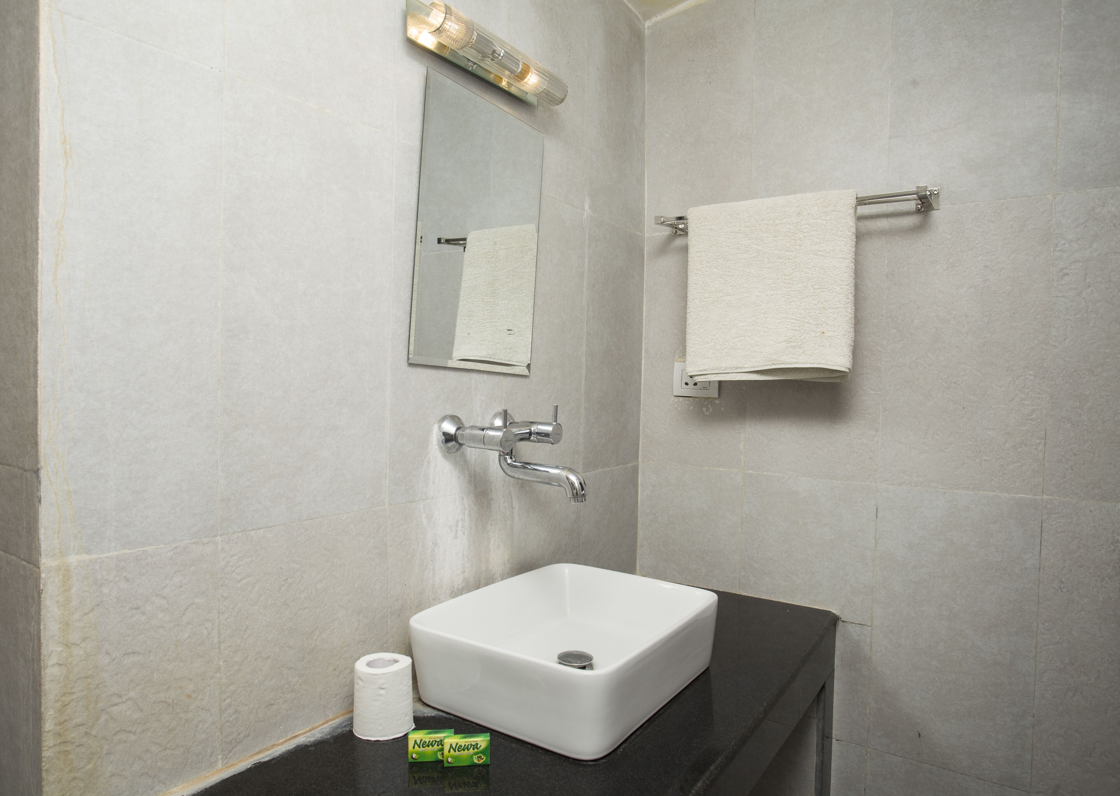 Un baño con lavamanos blanco, un espejo, toallero y un rollo de papel higiénico.