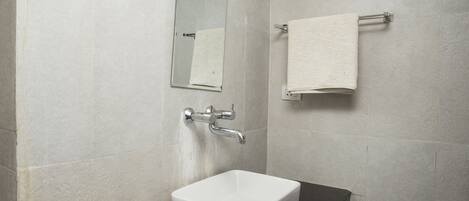 Un baño con lavamanos blanco, un espejo, toallero y un rollo de papel higiénico.