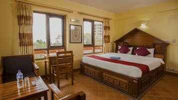 A hotel room with a wooden bed, a desk with a chair, and a window with curtains.
