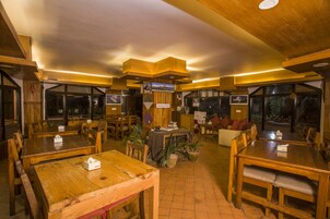 Un restaurante con mesas y sillas de madera, una estación de carga y amplios ventanales.