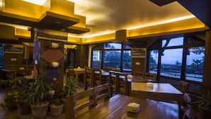 Ein Restaurant mit Holztischen, großen Fenstern und Zimmerpflanzen.