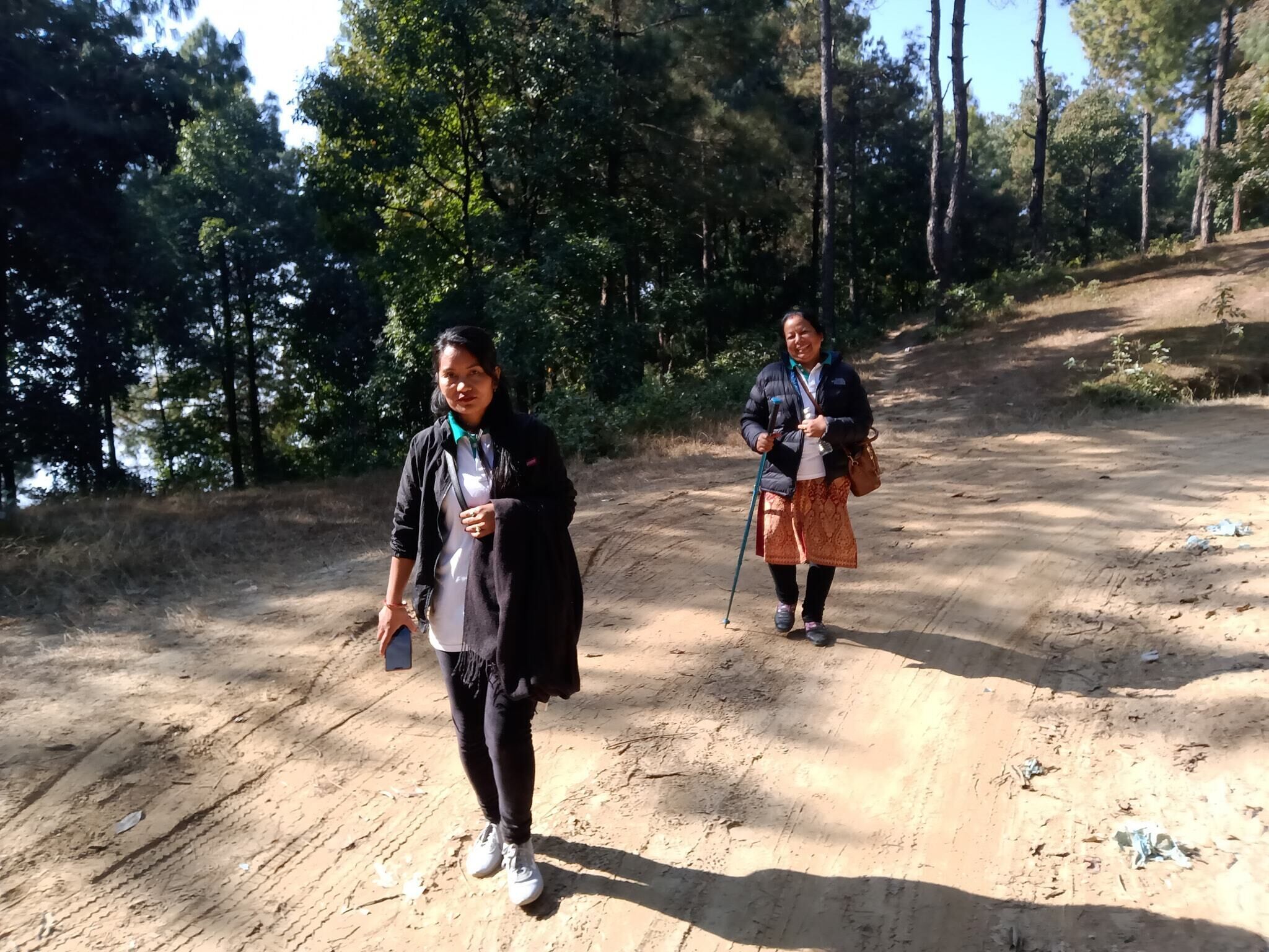 Dos personas caminando por un sendero de tierra en un área boscosa.