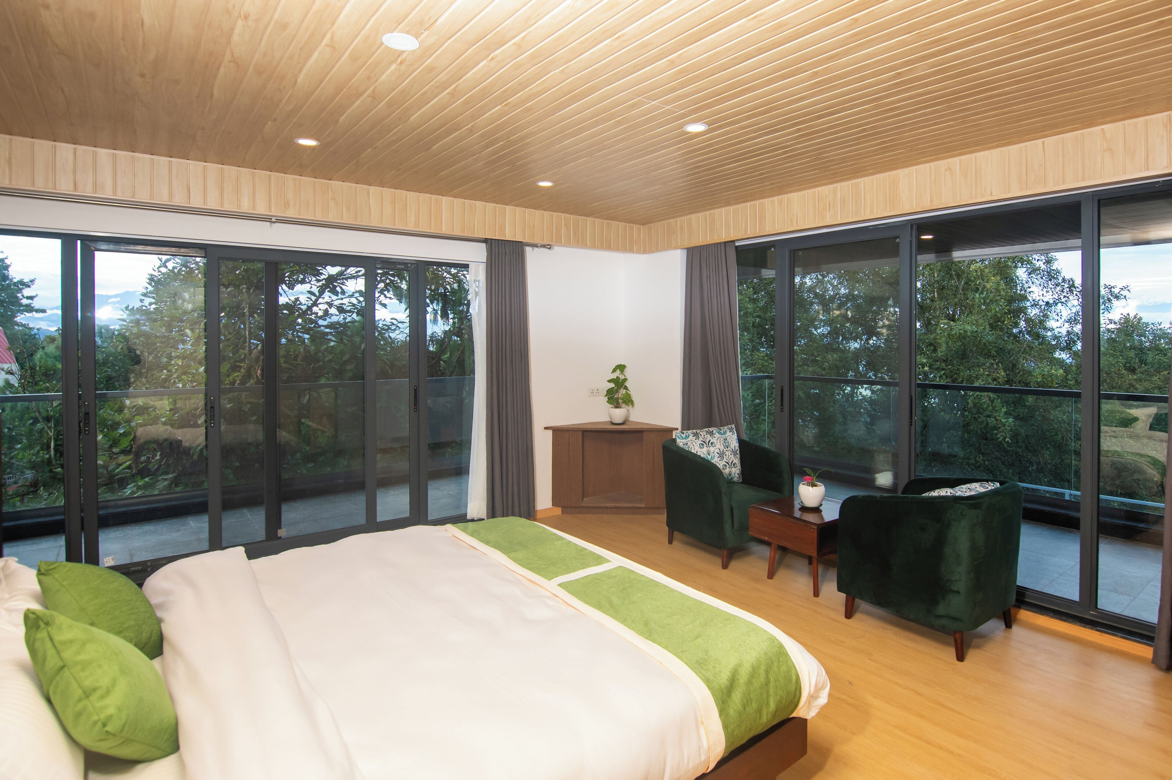 A modern bedroom with a large bed, a green armchair, and a small table with a plant.