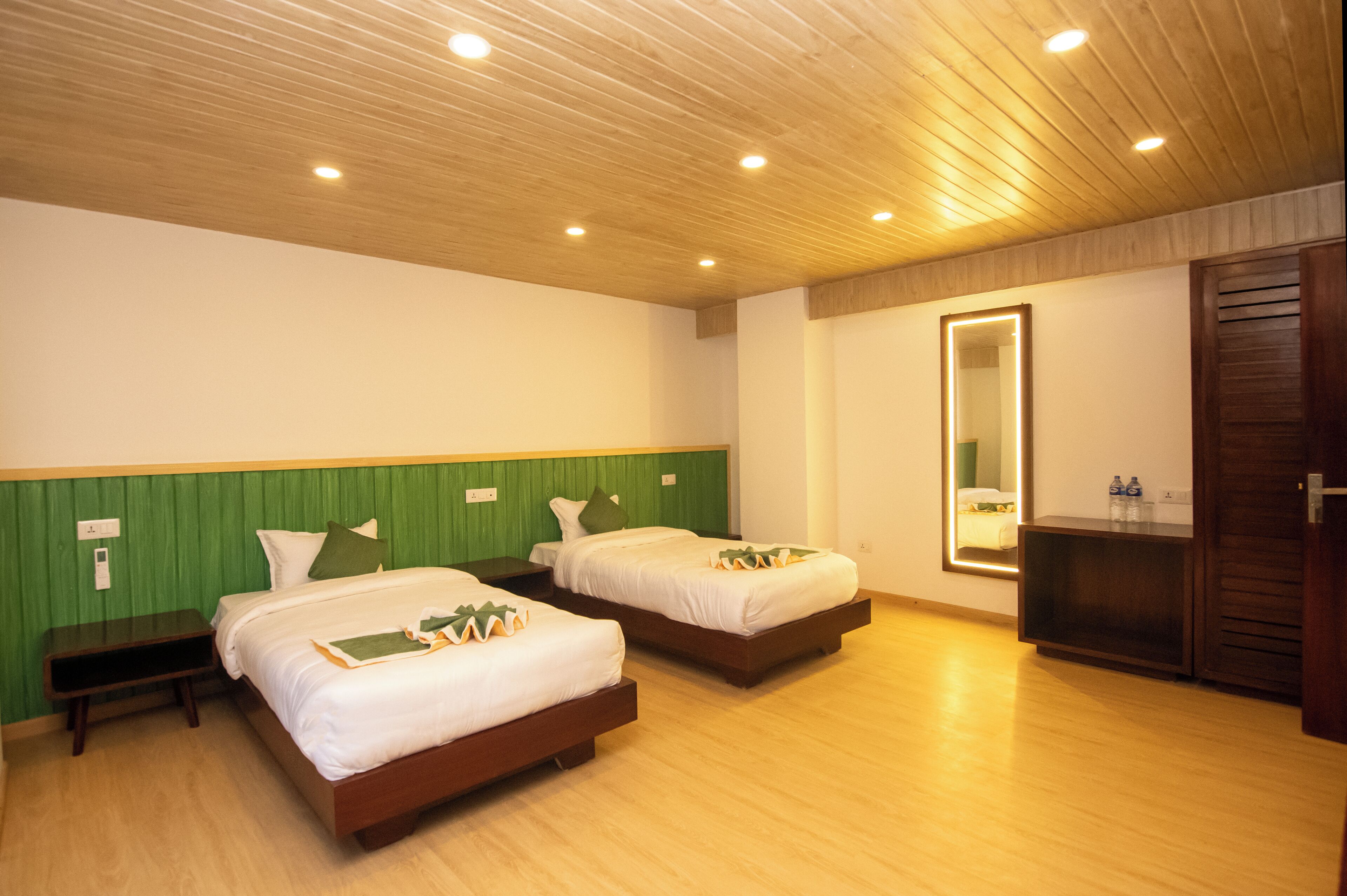 A hotel room with two beds, a green headboard, a wooden ceiling, and a mirror with a light.