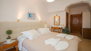 Habitación de hotel con una cama grande, una mesita de noche con lámpara, una planta pequeña en maceta y un espejo sobre el tocador.