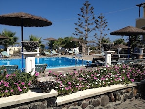 A pool area with lounge chairs, umbrellas, and a stone wall with flowers. - Santa Elena (Santorini)