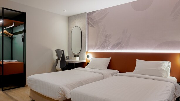 Een hotelkamer met twee bedden, een bureau, een stoel, een kast en een grote spiegel.