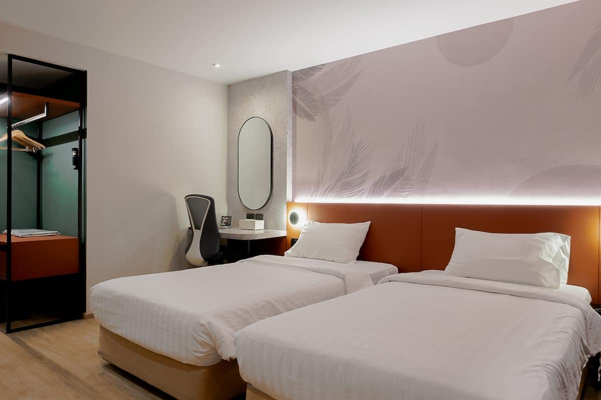 Une chambre d’hôtel avec deux lits, un bureau, une chaise, une armoire et un grand miroir.