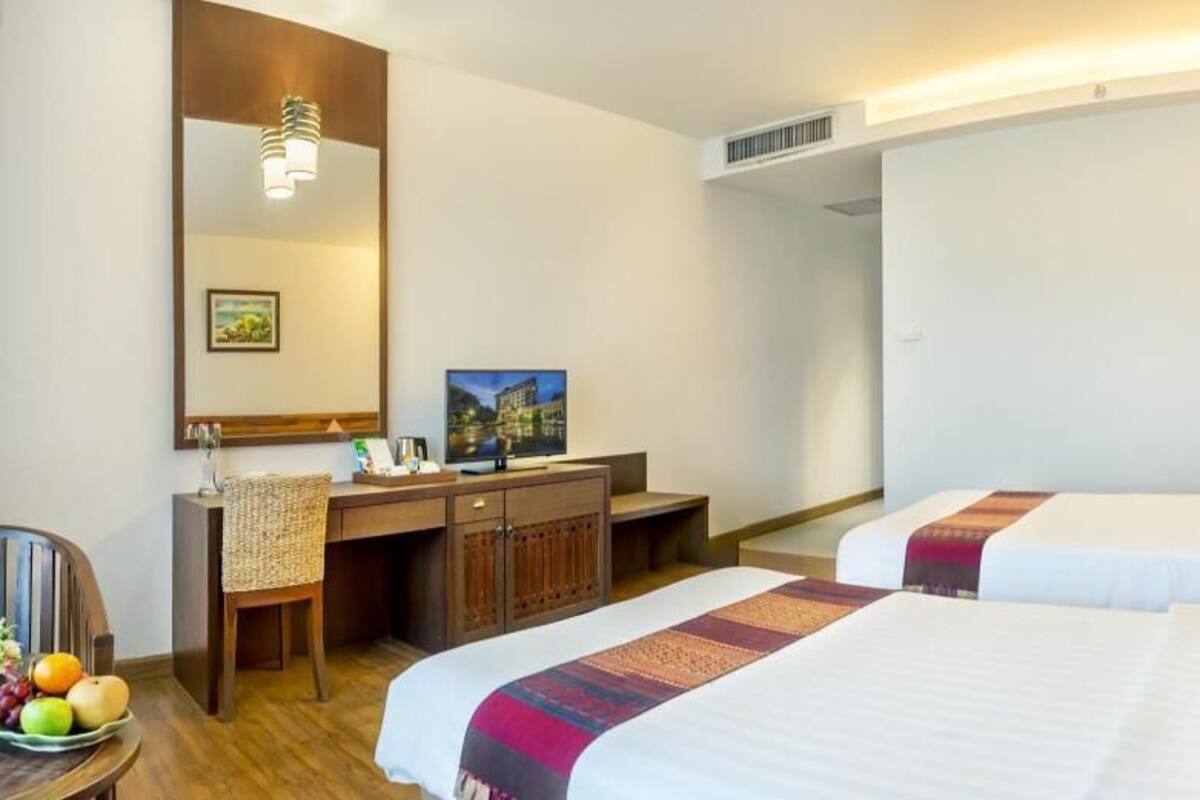 Une chambre d’hôtel avec deux lits, un bureau, une chaise, un miroir et un téléviseur.
