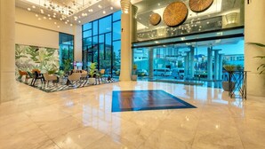 Een ruime lobby met een gepolijste marmeren vloer, grote ramen en moderne verlichtingsarmaturen.