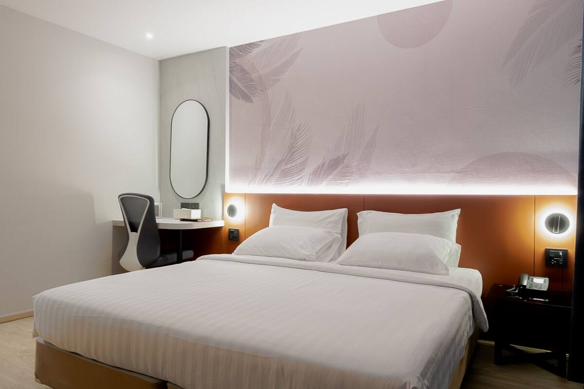 Une chambre d’hôtel moderne avec un grand lit, un bureau avec une chaise, un miroir et une table de chevet avec un téléphone.