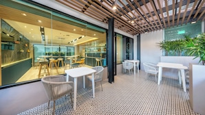 Een moderne hotellobby met diverse zithoeken, waaronder tafels en stoelen, en een zichtbare keuken in de achtergrond.